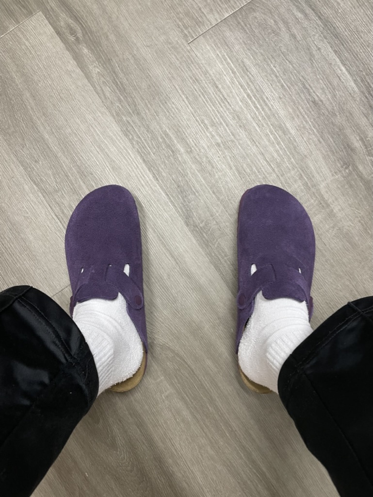 Purple Birkenstock clogs worn with white socks, standing on a wood floor.