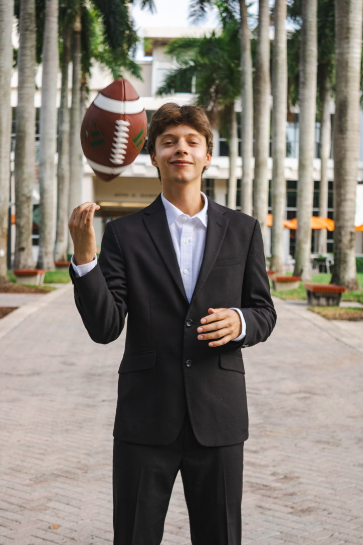 Bruno tossing a football on UM's palm-lined campus, dressed in a suit.