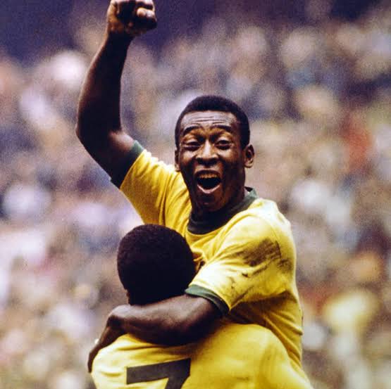 An older Pelé smiling and holding replica World Cup trophies.